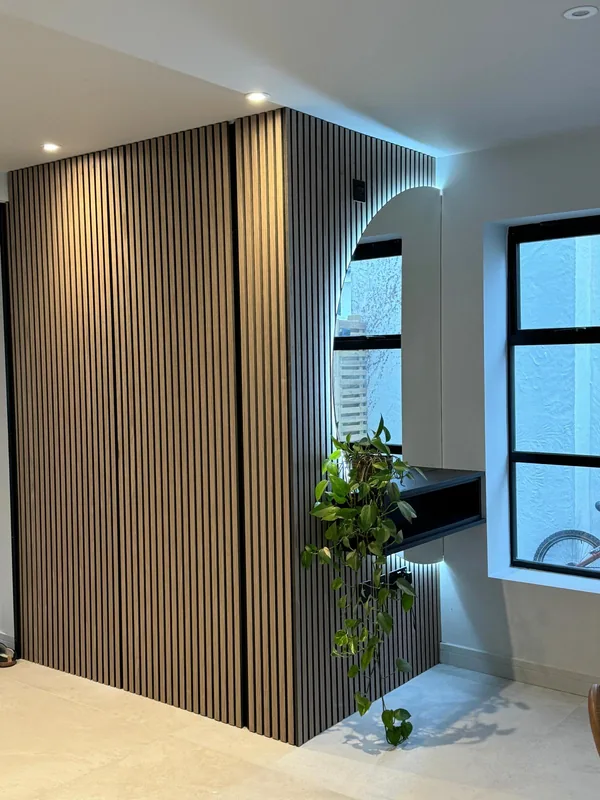 A hallway wall in oak and black fluted panelling with an arched mirror and a floating black shelf