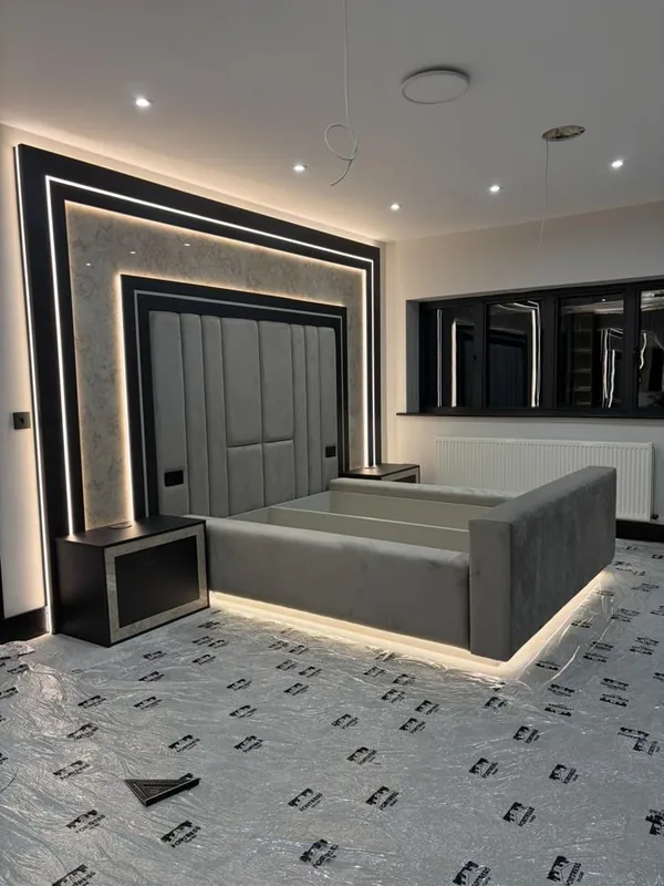 An upholstered bed with a lit headboard set into a stone-effect panel, framed in concealed LED, with floating bedside cabinets